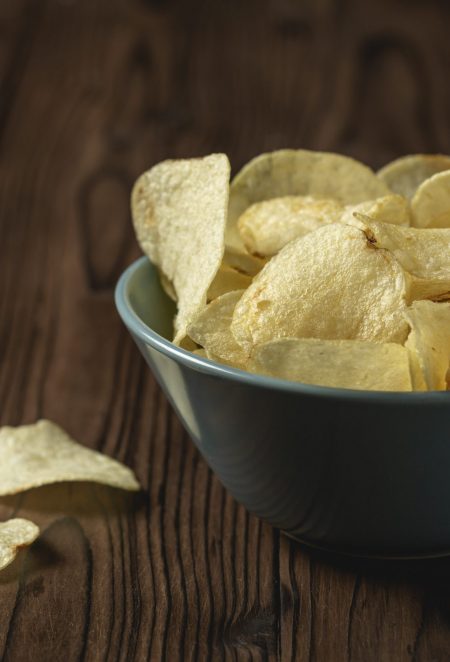 Potato chips in bowl on a wooden table.